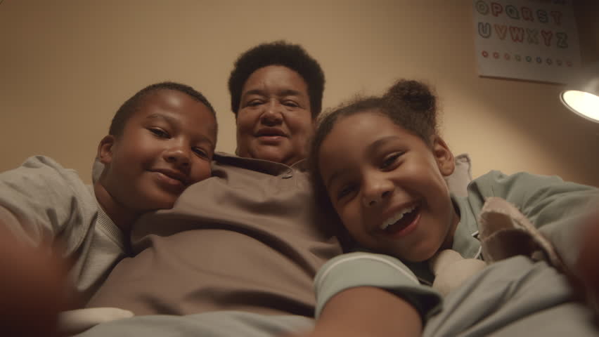 Handheld POV of cheerful African American tween kids recording video of themselves and their happy grandma having fun together in bed at night Royalty-Free Stock Footage #1111009989