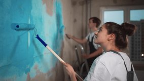 Happy couple in working clothes renovating new house apartment painting wall together in blue color using paint rollers. Home makeover, renovation concept. Family man woman repair flat themselves. - Powered by Shutterstock - Get 15% off with code: PIKWIZARD15