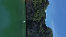 Beautiful white yacht near a tropical island in Thailand, a sailing catamaran near the rocks in the sea, view from a drone -vertical 4k video