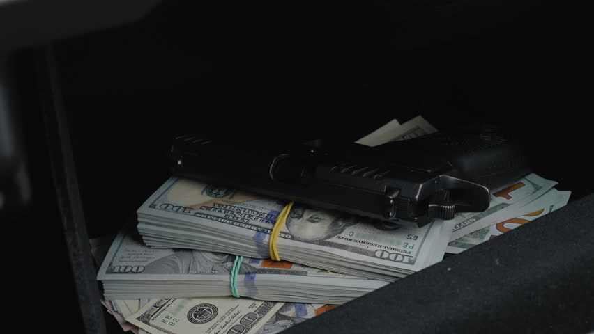 Close up a male pulling out a concealed handgun and a large sum of money from a car glove box compartment