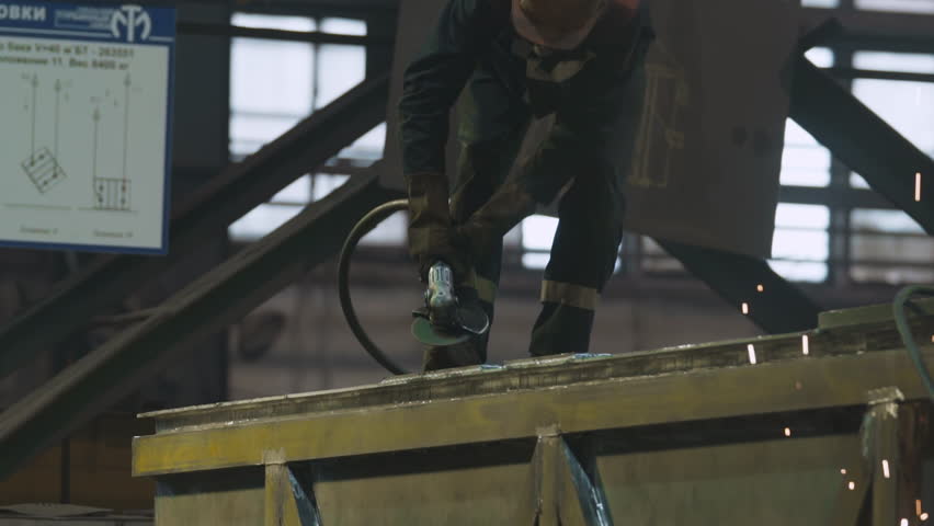 Grinder in the hard hat producing heavy industry items at the plant. Professional grinder manufacturing heavy products. Grinder scraping off the metal from the heavy product in a workshop. Royalty-Free Stock Footage #1111014251