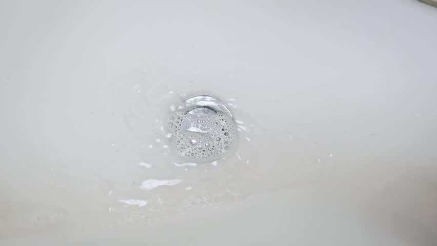 Water drains into the sink in the bathroom and swirls in slow motion. Inside view of spinning water in the modern bathroom. Top view, camera rotating. The water stream goes down the sewage. Royalty-Free Stock Footage #1111018063