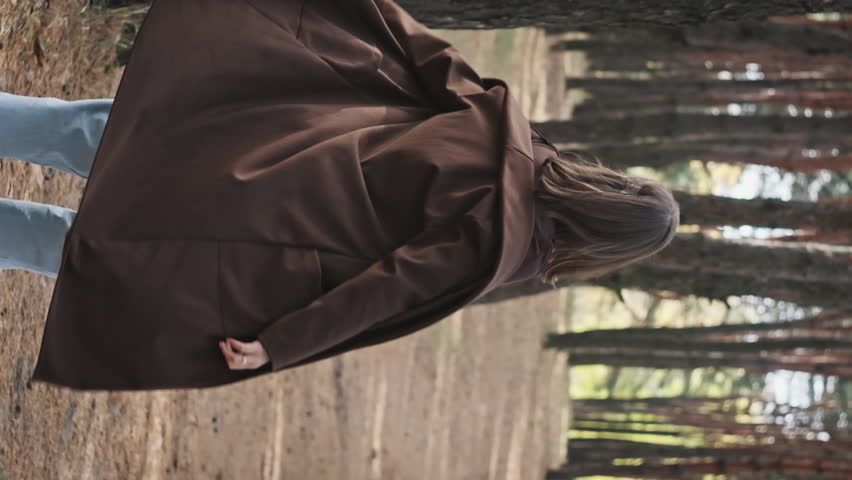 Vertical Pretty young woman spins in the pine forest, slow motion. Joyful girl, enjoying life in nature, posing, dancing happily, looking around, enjoying life. Mood of freedom, romantic. Lifestyle