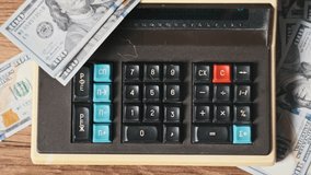 Top view counting on an old vintage calculator surrounded by dollars, close-up. Male hand press keyboard buttons on retro calculating machine on wooden desk. Finances, currency, savings, bills. 4K - Powered by Shutterstock - Get 15% off with code: PIKWIZARD15