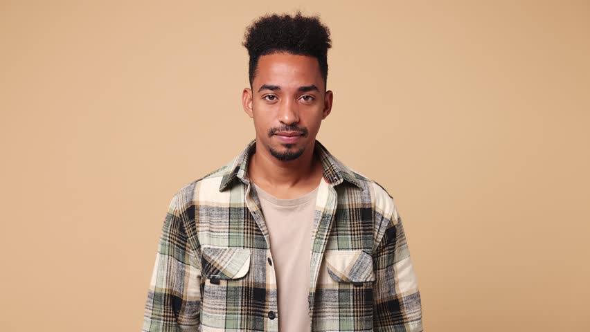 Hesitant indecisive fun shy young man of African American ethnicity wear shirt casual clothes feels doubtful spreading hands say oops ouch oh omg i am so sorry isolated on plain beige brown background Royalty-Free Stock Footage #1111018983