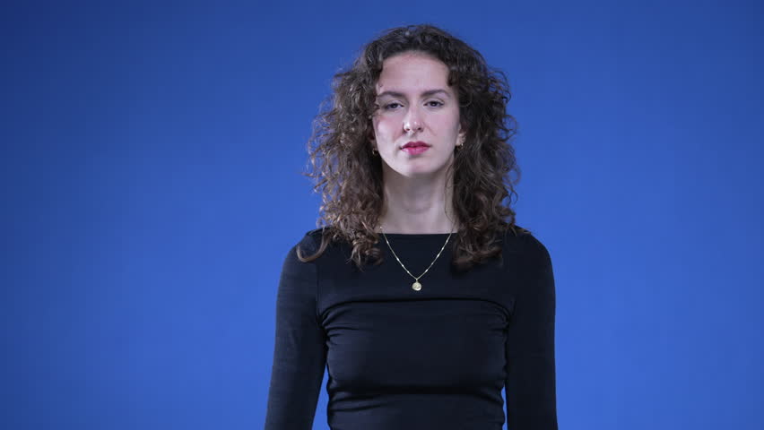 Woman pointing at herself in confusion with finger in disbelief and consternation standing on blue background. 20s person reacting to accusation Royalty-Free Stock Footage #1111020617