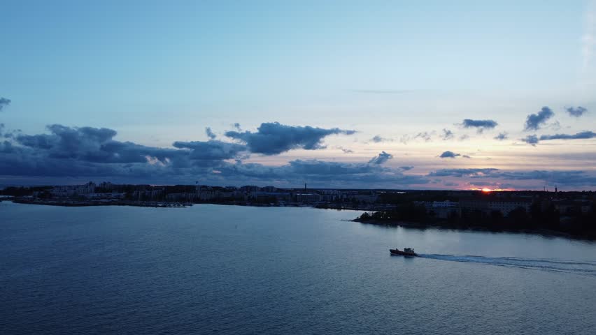 Fishing vessel motors on sea as sun sets over deep blue Helsinki, FIN