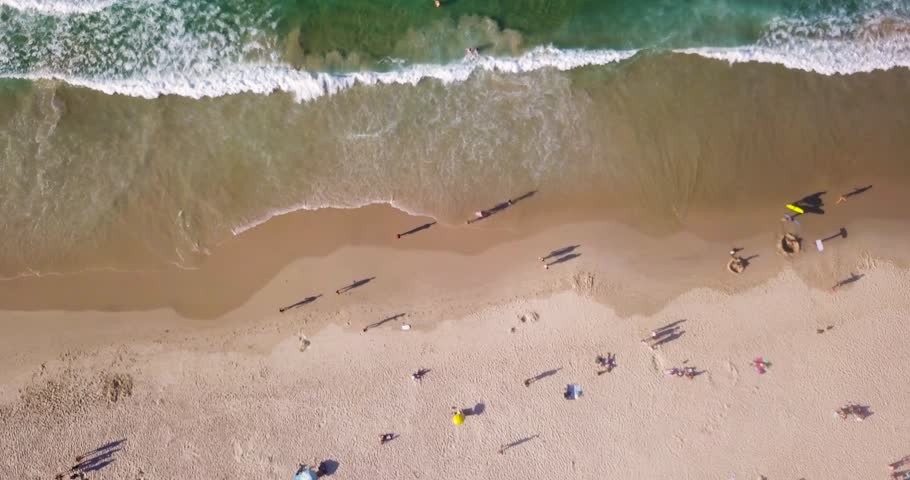 Tourists roam across golden sand of Byron Bay beach Australia on sunny day, aerial top down