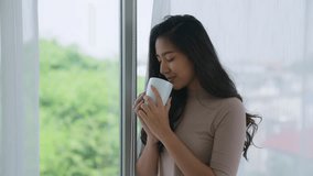 Side view of portrait pensive young asian woman standing by window curtains with cup of coffee at home. A girl drinking hot tea looking outside at autumn landscape copy space relaxing and enjoying. - Powered by Shutterstock - Get 15% off with code: PIKWIZARD15