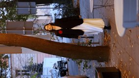 a beautiful woman in a black jacket with a red flower on her chest and a white dress walks in the evening city against the background of the street and cars. vertical video. business woman
