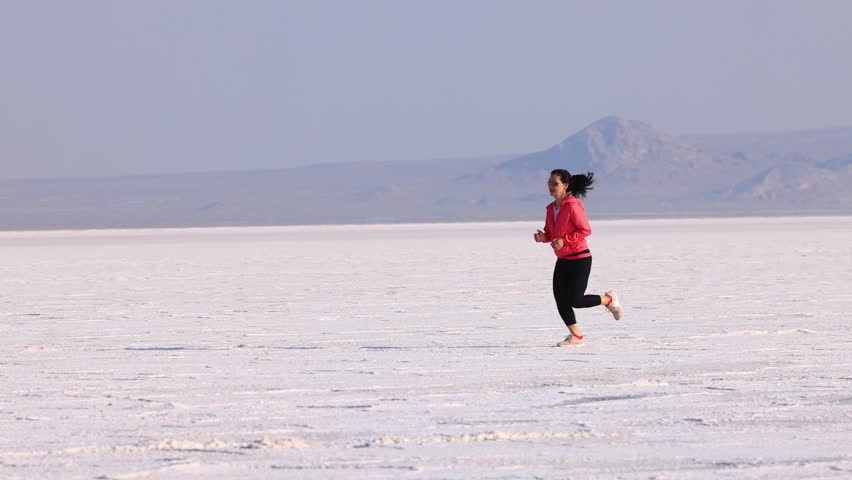 Asian woman jogging across the Bonneville Salt Flats flats in Utah.