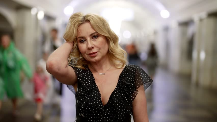 portrait of romantic middle-aged woman in metro, crowds of people walking in blurred background