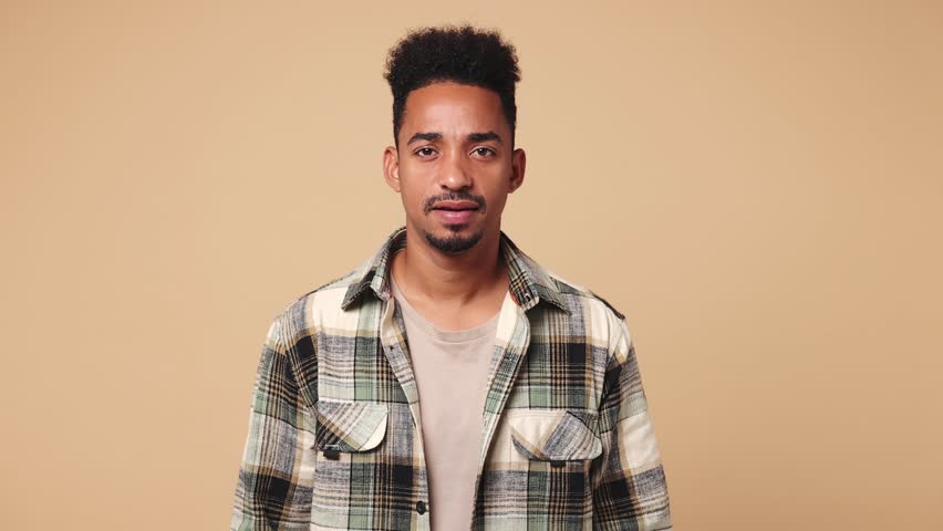 Young displeased man of African American ethnicity he wear shirt casual clothes ask what hears fake news propaganda has some problems gesticulating with hands isolated on plain beige brown background | Shutterstock HD Video #1111038453