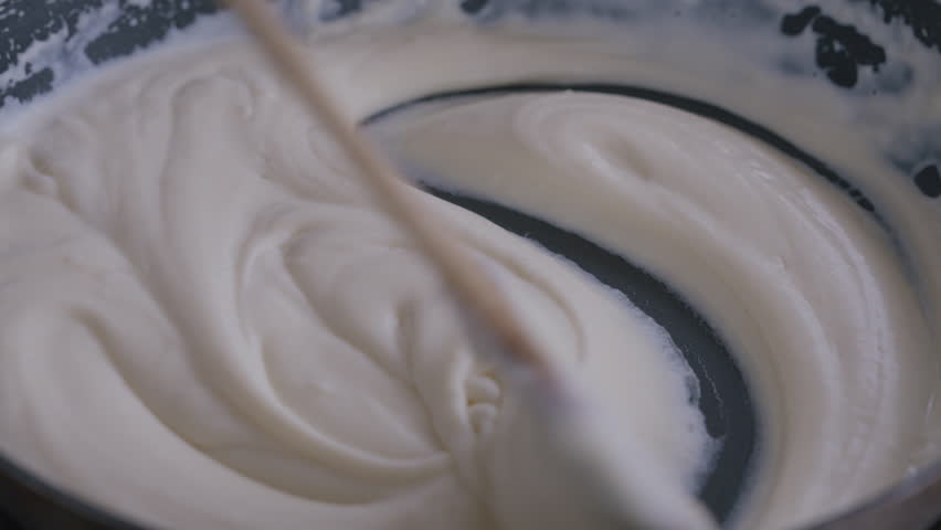Close-up making béchamel sauce. Stirring in pan with wooden spoon. Béchamel for macaroni and cheese or lasagne. Beautiful kitchen homemade food. Close-up shot in 4k, 50 or 25 frames per second. Royalty-Free Stock Footage #1111038885