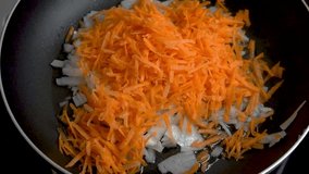 Freshly grated carrots and onions are fried in a pan. Close-up. Slow motion video. Cooking master class. Home cooking.