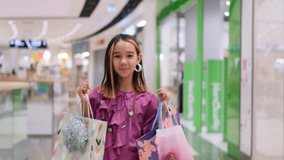 Little fashion girl with packages in a large shopping center. Pretty smiling little girl with shopping bags posing in the shop