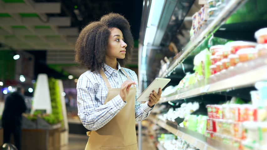 African american employee clerk working on tablet, checking condition of product in a grocery store market near shelves Black woman, manager checks the expiration date inventory in supermarket