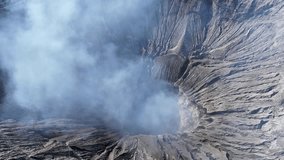 Aerial 4K footage of the Bromo volcano crater caldera with smoke coming. An active volcano in Tengger Semeru National Park in East Java, Indonesia.