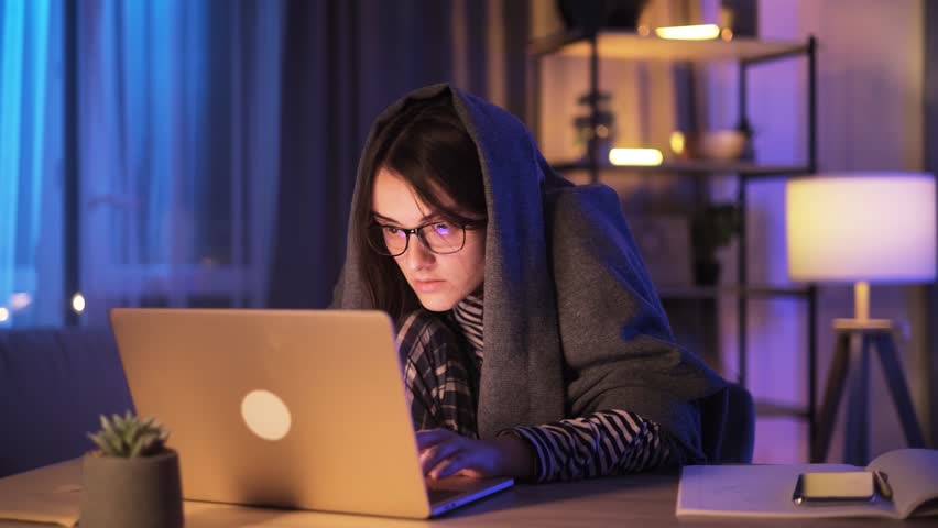 Anxious paranoid young woman nervously typing on a laptop scrolling through news or social media feed looking around so that no one is spying at late night at home workplace Addiction concept