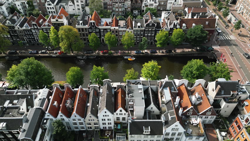 Top view of rows of stunning sharp roofs and facades of high modern buildings of Amsterdam separated by long narrow canal with moored boats. High quality 4k footage