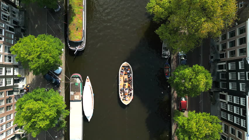 Canal cruise on a sunny summer day. Aerial view of amazing landscape of narrow treelined canal with moored boats, facades of modern buildings on the sides. High quality 4k footage Royalty-Free Stock Footage #1111046245