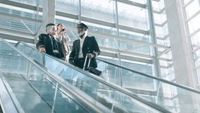 Escalator, pilot and people at airport for travel, talking and conversation. Mature, captain and black man and woman in communication, speaking together or discussion at lobby with suitcase luggage - Powered by Shutterstock - Get 15% off with code: PIKWIZARD15