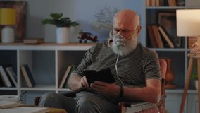Old man in breathing mask stay in chair and read book. Old man is using nebuliser because of hard breathing. Theme of medical curation of various lung diseases. - Powered by Shutterstock - Get 15% off with code: PIKWIZARD15