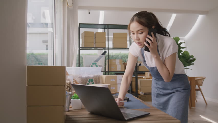 Young woman asia people SME owner apron busy work phone call check list prepare stock sale order box at eco green home office desk online shop store. Supply chain smart asian vendor seller service job Royalty-Free Stock Footage #1111055373