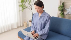 Asian middle aged woman in pajama using the laptop in the living room