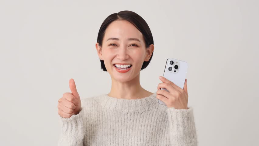 Asian middle aged woman with the smartphone thumbs up gesture in white background Royalty-Free Stock Footage #1111058553