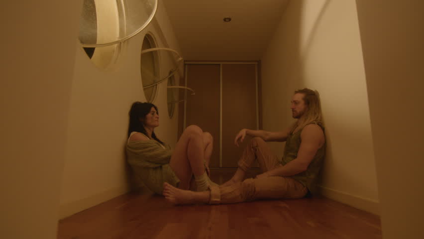Young depressed couple sitting on the floor in corridor with flashing light, looking at each other emotionlessly, feeling exhausted after conflict. Zoom-out Shot | Shutterstock HD Video #1111061241