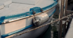 Detailed closeup shot of cylinder buoy hanging from metal clips on side of white and blue wooden boat lit by golden hour light