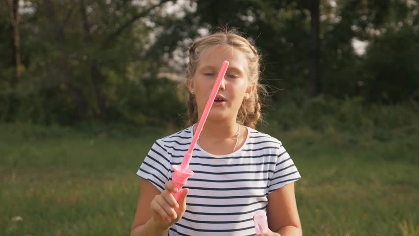 Cute little girl blowing soap bubbles. Carefree happy kid is playing in the park. Kid funni play emotions, dream in the park with soap bubbles.Concept happy family children