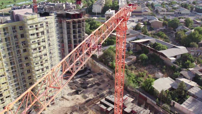 Drone flies over construction crane among apartment buildings under construction on summer day