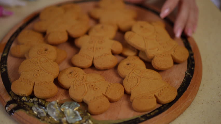 Slow motion. Close-up of freshly baked Christmas gingerbread cookies. Female hands lay out gingerbread men on a round wooden board