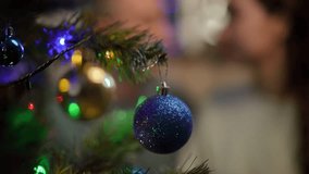 Slow motion. Close-up of a blue Christmas ball on a Christmas tree branch. In the background, a kissing couple is out of focus - Powered by Shutterstock - Get 15% off with code: PIKWIZARD15
