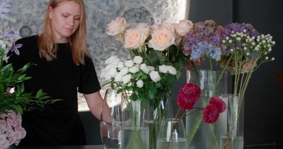 The florist assembles an arrangement of flowers for a customer in her store | Shutterstock HD Video #1111072127