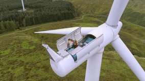 Steady aerial drone closemid shot showing anonymous worker fixing and maintaining wind turbine, cloudy day, forest surroundings.  - Powered by Shutterstock - Get 15% off with code: PIKWIZARD15