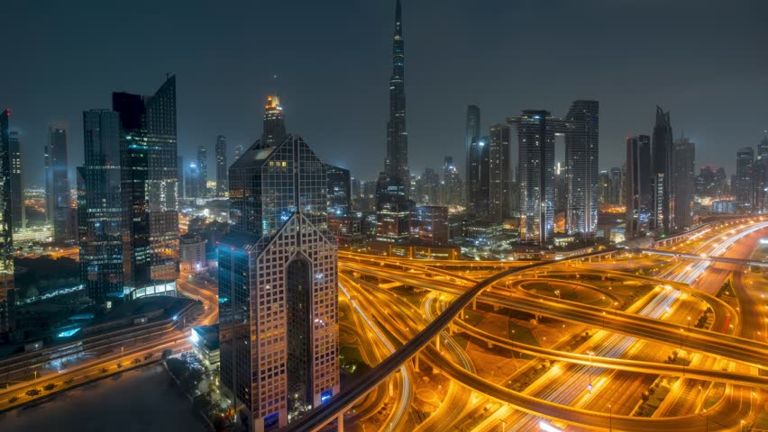 Moody night to day timelapse view of skyline of Downtown Dubai and busy Sheikh Zayed road intersection, United Arab Emirates, with clouds and rain