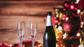 hand with champagne bottle filling two glasses with christmas tree background with out of focus gifts