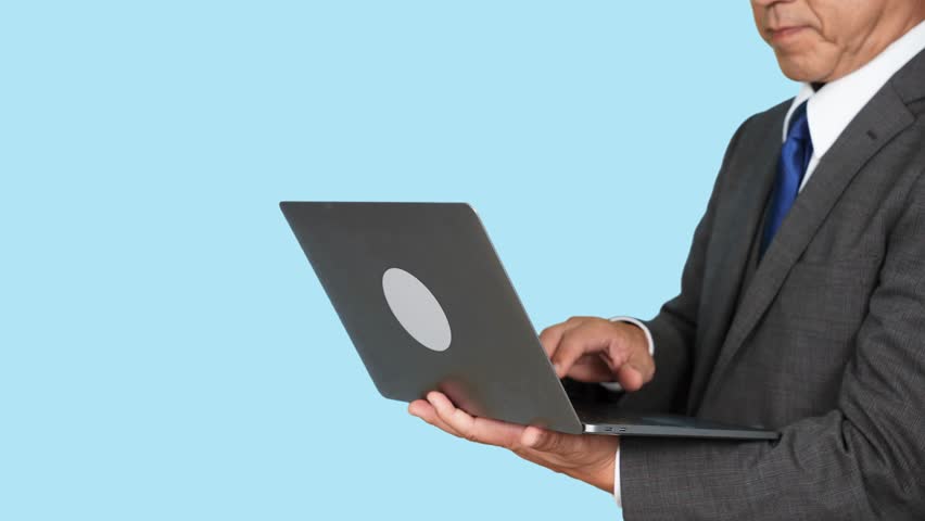 Asian middle-aged man in a business suit using a laptop PC in front of a blue background. Royalty-Free Stock Footage #1111079603
