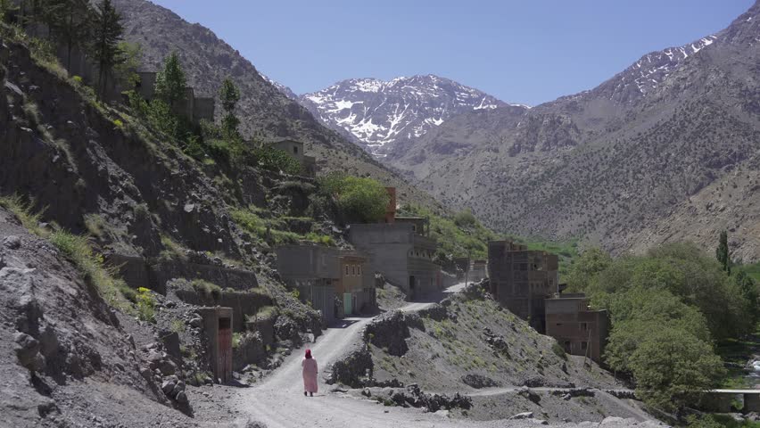The woman walking along the rural road on the hillside. Imlil, Morocco.