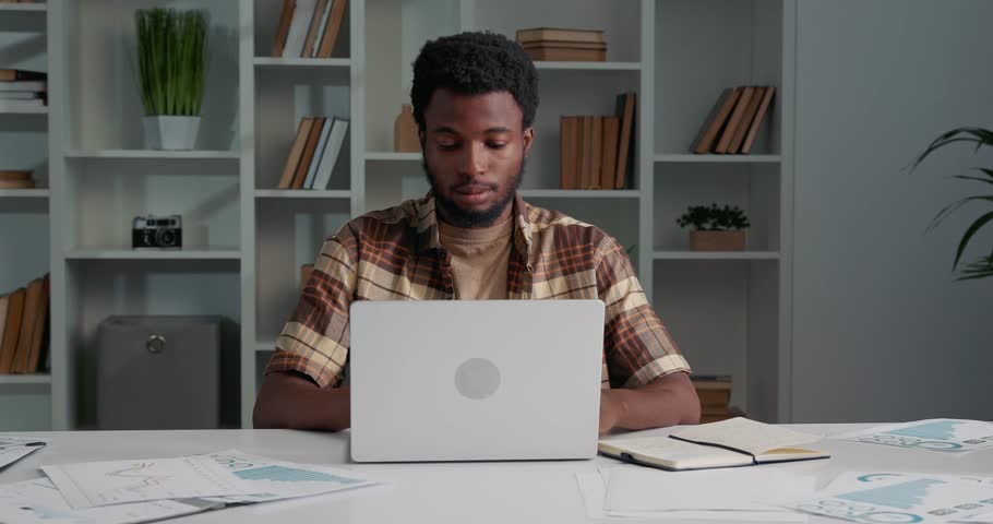 African man sitting at the office, hardworking, looking tired and stressed. Manager having headache after work on laptop, he needs relax and rest. Man working with paper documents. | Shutterstock HD Video #1111086821