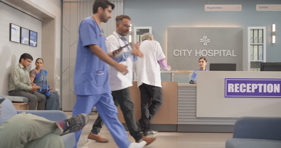 Tracking Dolly Shot of Hospital Corridor and Lobby Filled with Group of Diverse Indian Patients Waiting for their Appointments. Modern Health Clinic with Active Doctors, Nurses and Staff Working Royalty-Free Stock Footage #1111088999