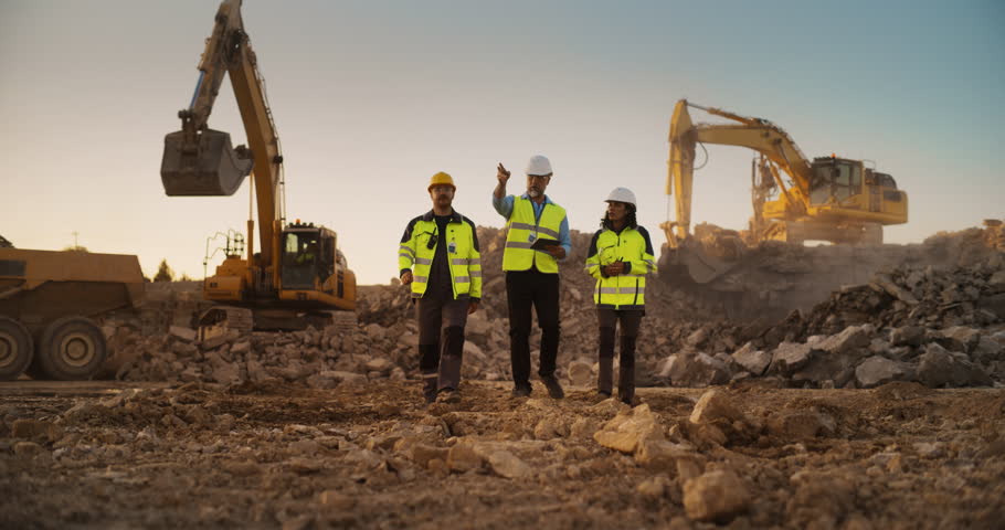 Construction Site With Excavators on Sunny Day: Diverse Team Of Male And Female Specialists Walking And Discussing Real Estate Project. Civil Engineer, Architect, Urban Planner Talking, Using Tablet.