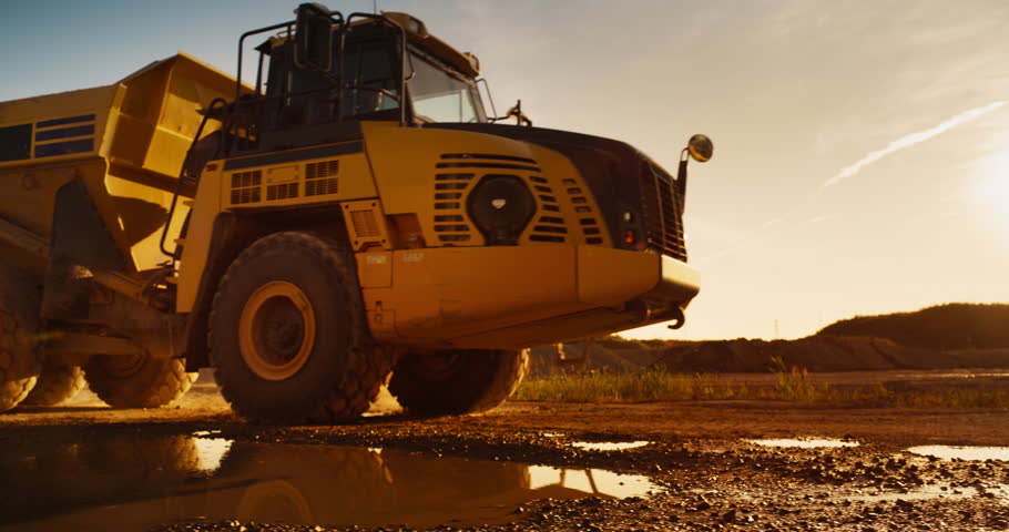 Construction Site On A Hot Sunny Day: Industrial Truck Driving To Load Material Necessary For Building New Apartment Complex. Worker Operating Heavy Machinery To Complete A Real Estate Project.