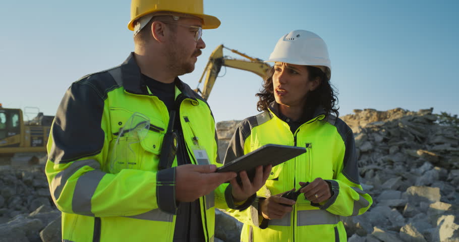 Caucasian Male Civil Engineer Talking To Hispanic Female Inspector And Using Tablet On Construction Site of New Apartment Building. Real Estate Developers Discussing Business, Excavators Working. Royalty-Free Stock Footage #1111090629