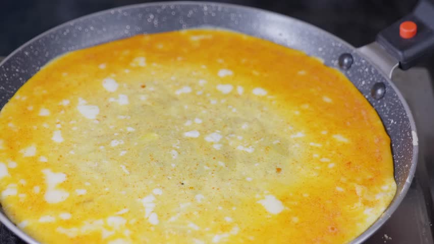 scrambled eggs mixture with spices spreading in the pan for omelet cooking in gas burner stove