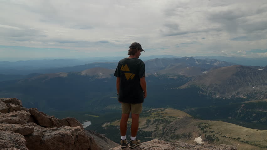 Cinematic man person at the top of Rocky Mountain National Park Colorado Denver Boulder Estes Park 14er Longs Peak looking out to Indian Peaks sunny cloudy late summer dramatic landscape still