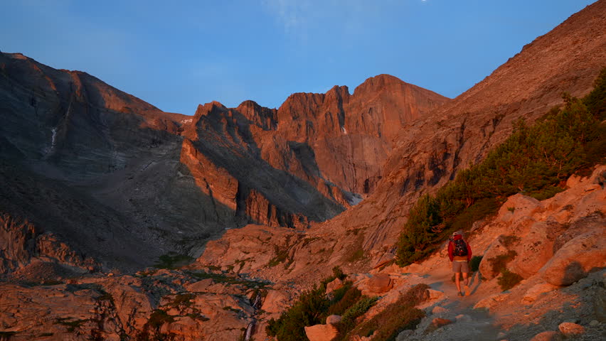 Cinematic first light sunrise orange red hiker Longs Peak 14er sunrise Rocky Mountain National Park above treeline Colorado Denver Boulder Estes Park summer dramatic landscape pan slowly left